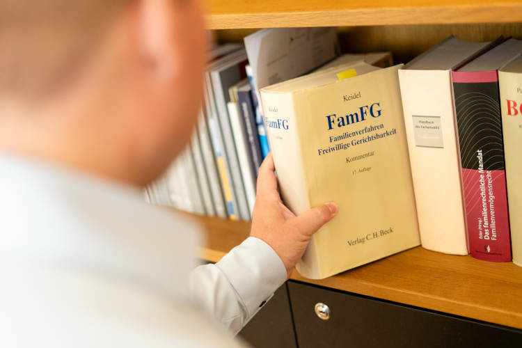 Eine Person hält ein Buch mit dem Titel "FamFG - Familienverfahren Freiwillige Gerichtsbarkeit" in einer Bücherregal.